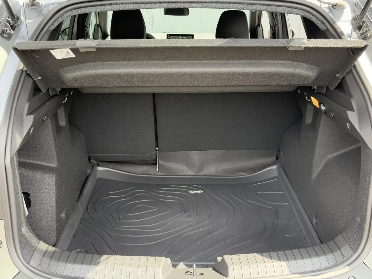 Coffre ouvert du Dacia Duster 2025 gris schiste, montrant le tapis de coffre noir et l'espace de rangement intérieur.