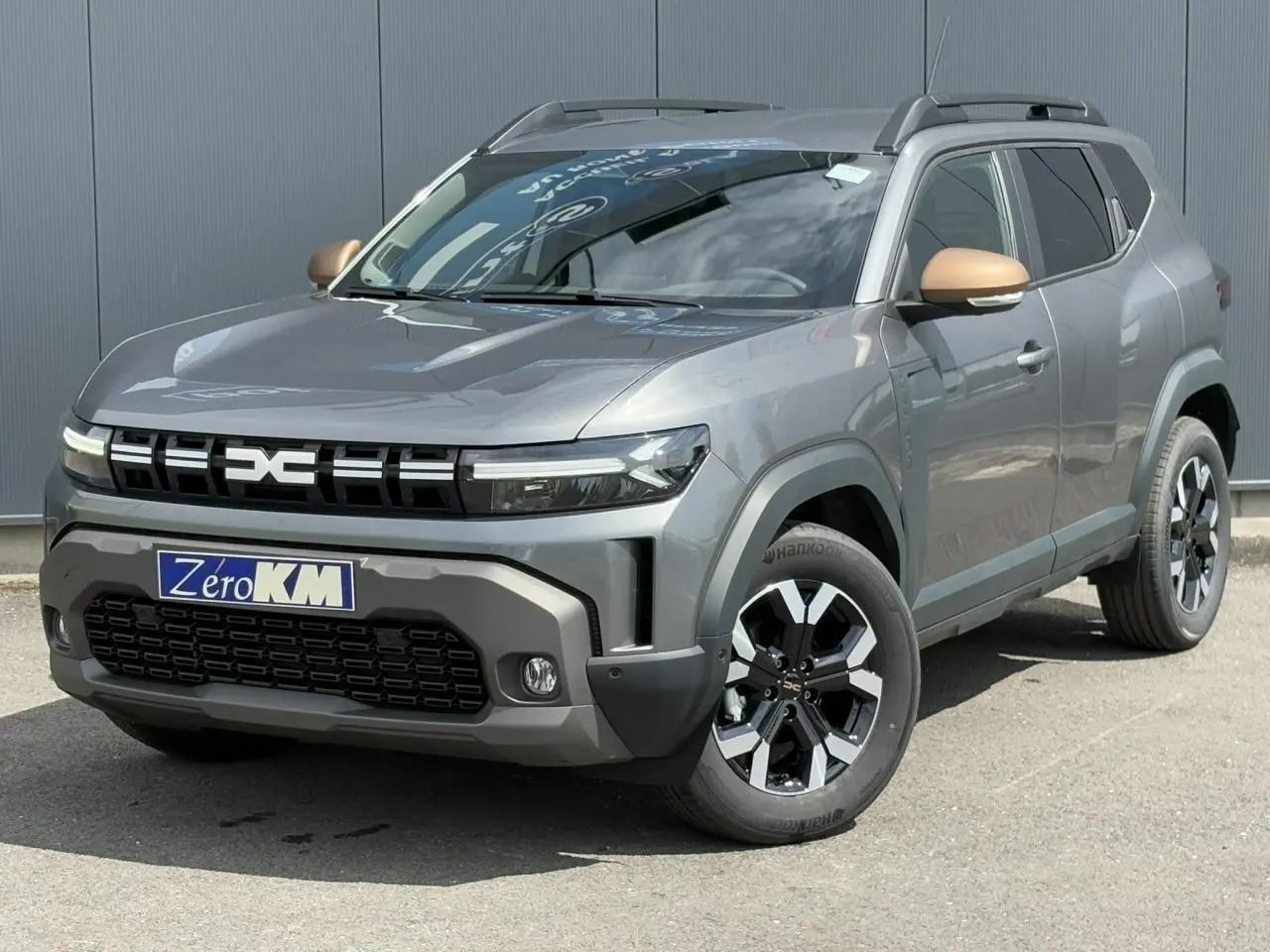 SUV Dacia Duster gris schiste en 3/4 avant droit avec coques de rétroviseurs brun cuivré et jantes alliage noires.