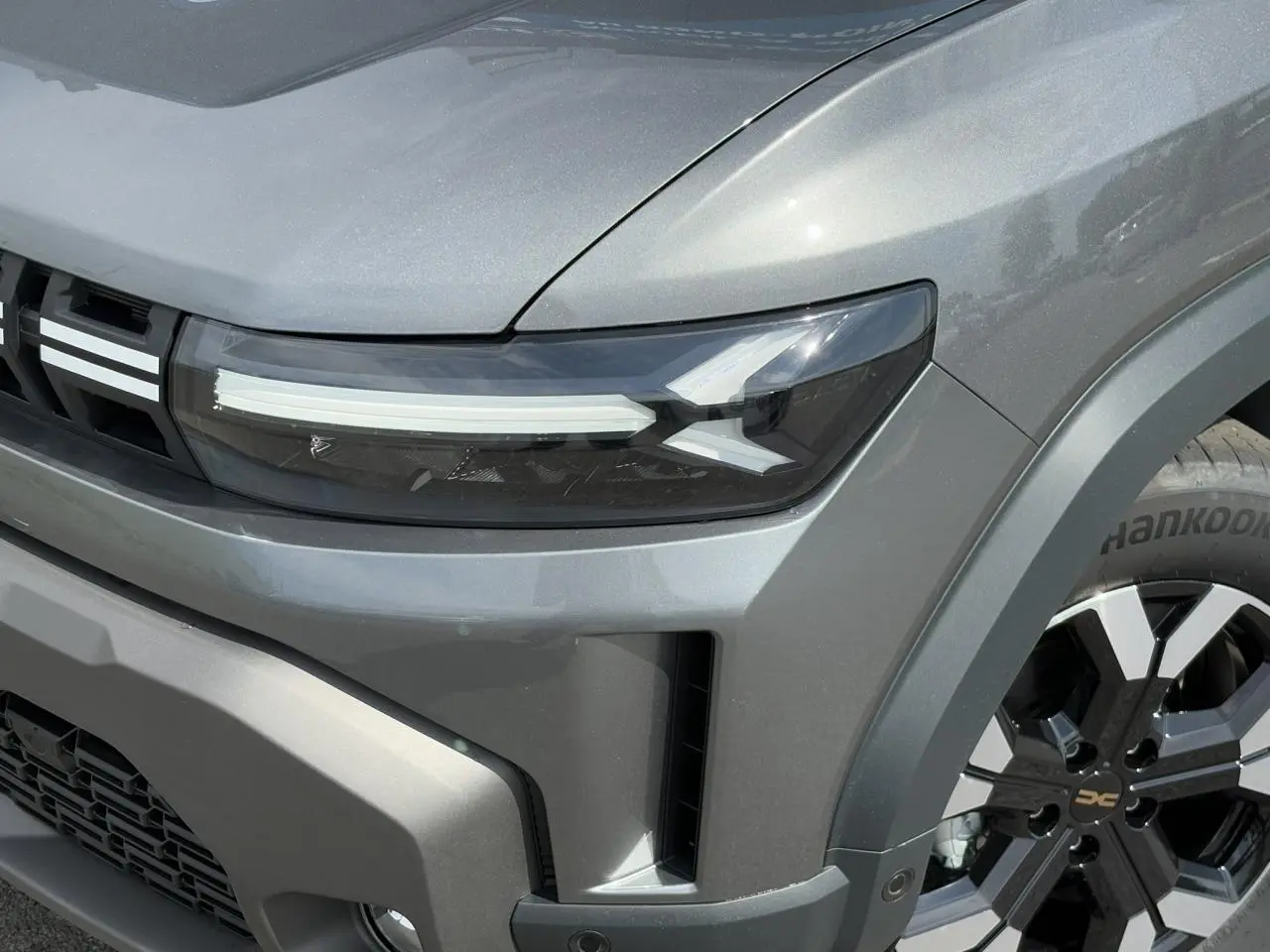 Gros plan sur l'avant droit du Dacia Duster gris schiste, mettant en valeur le phare LED et la jante alliage noire et argentée.