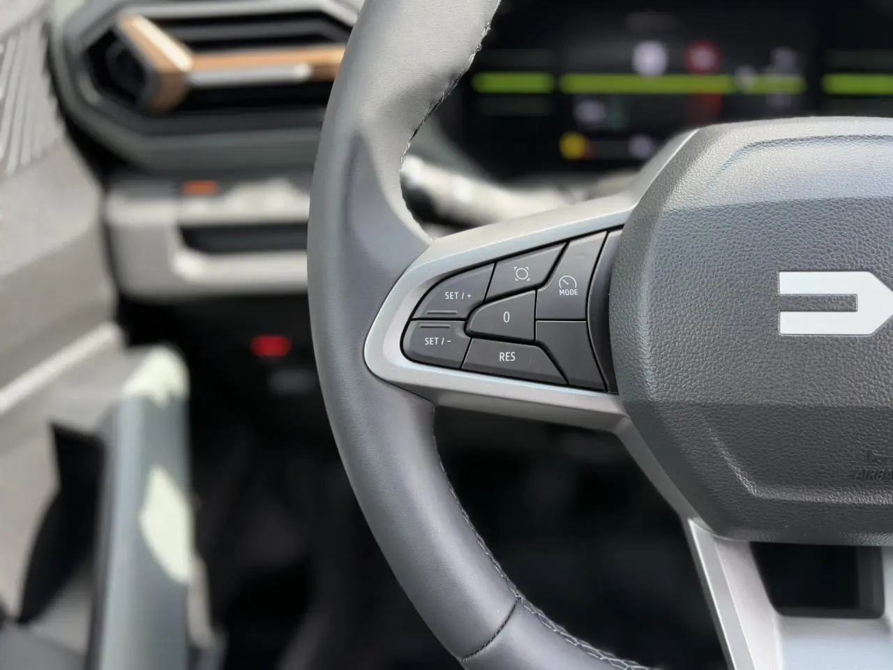 Gros plan sur le volant gris du Dacia Duster 2025, avec commandes intégrées et tableau de bord digital flou en arrière-plan.