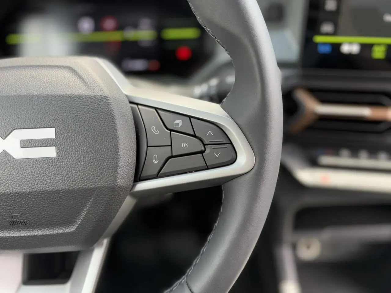 Gros plan sur le volant gris du Dacia Duster 2025, mettant en valeur les commandes multifonctions côté droit.