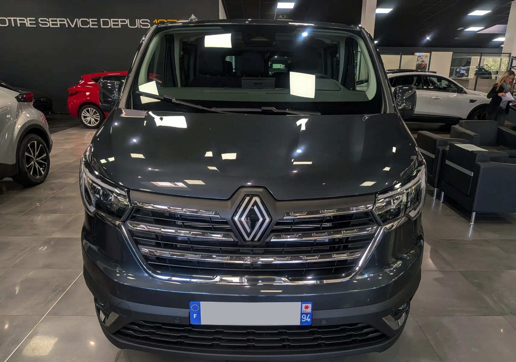 Vue frontale d'un Renault Trafic Combi gris comète 2025, mettant en valeur sa calandre chromée et ses phares LED.