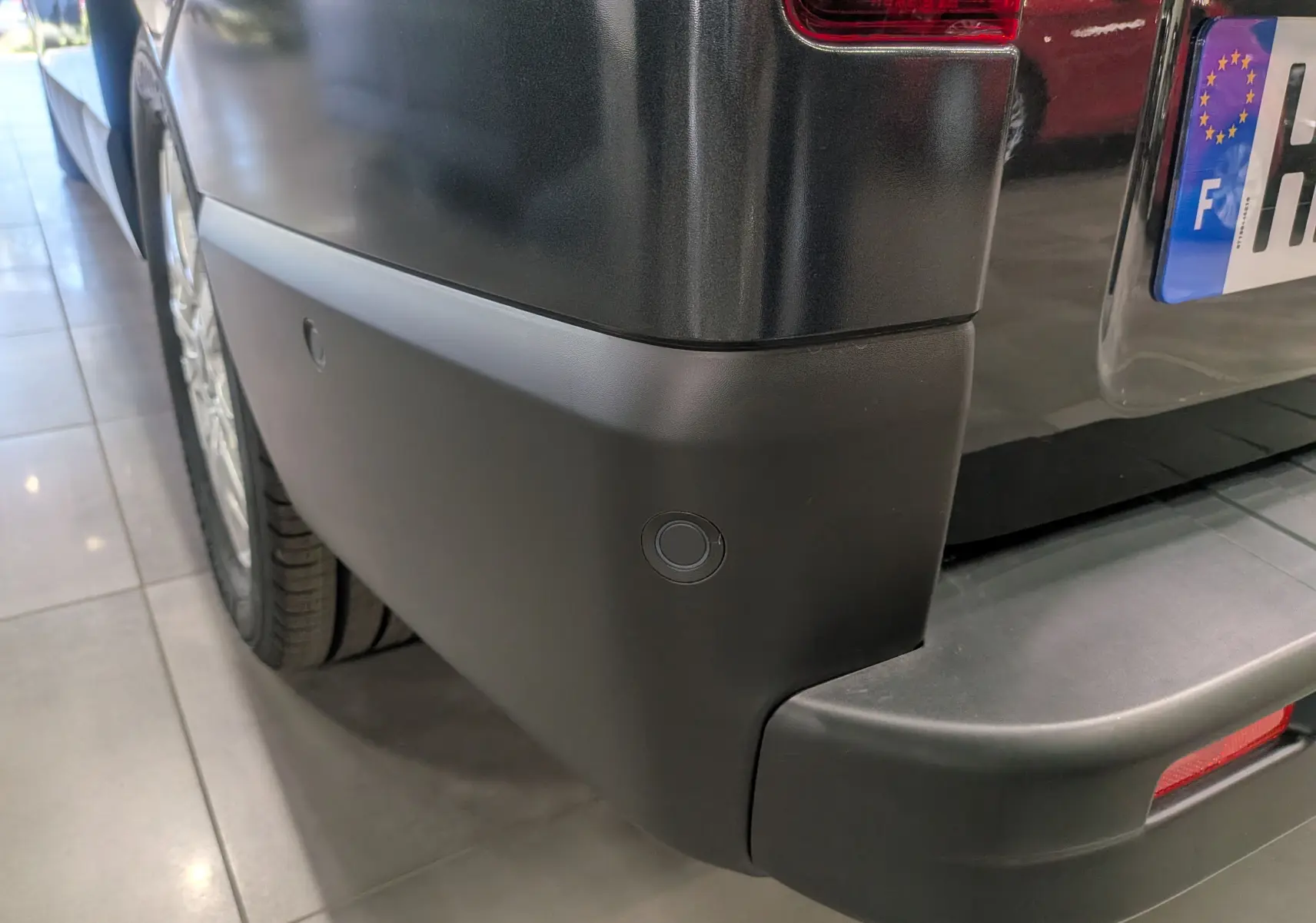 Gros plan sur le pare-chocs arrière gris comète du Renault Trafic Combi avec capteur de recul visible.