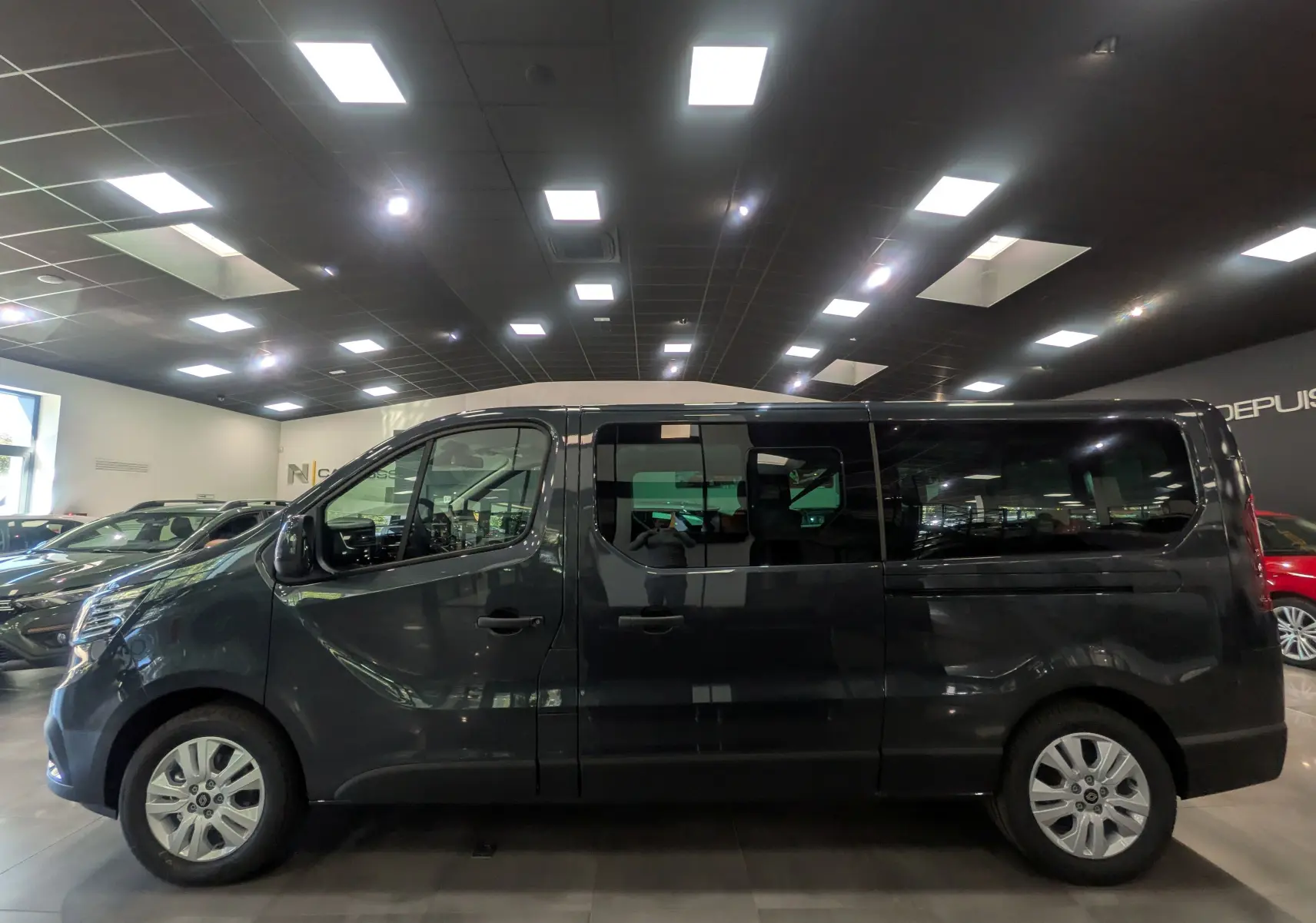 Profil côté gauche d'un Renault Trafic Combi gris comète 2025 en intérieur, avec vitres teintées et jantes alliage.