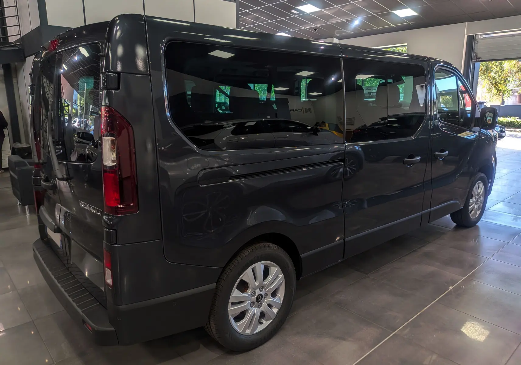 Renault Trafic Combi gris Comète vu en 3/4 arrière droit dans un showroom lumineux avec vitres teintées.