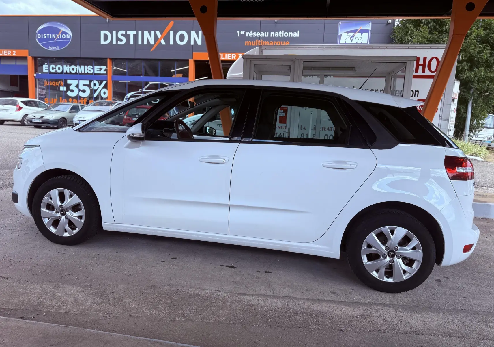 Profil côté gauche d'une Citroën C4 Picasso blanche de 2014, version 1.6 HDI Confort avec jantes alliage et toit noir.