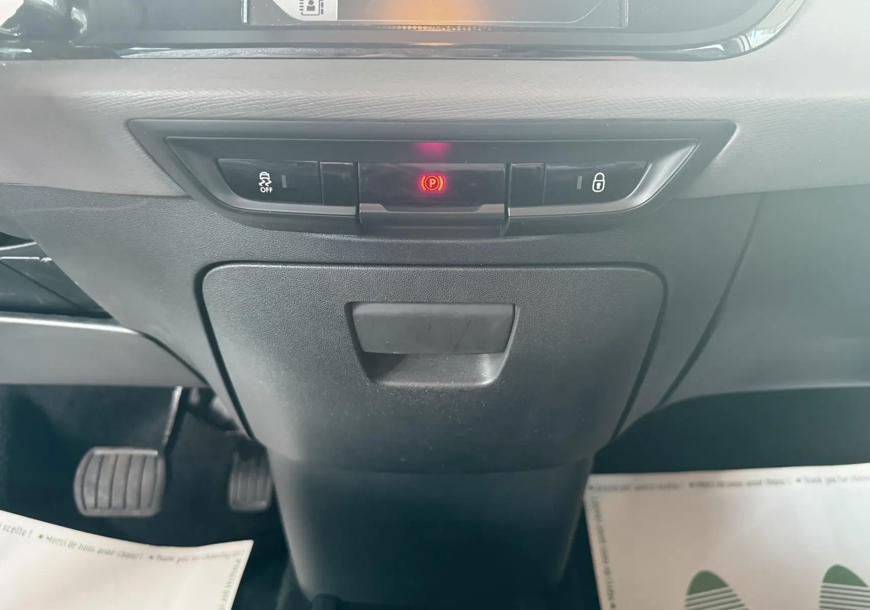 Vue rapprochée du tableau de bord central de la Citroën C4 Picasso blanc, avec commandes de frein à main électronique et verrouillage.