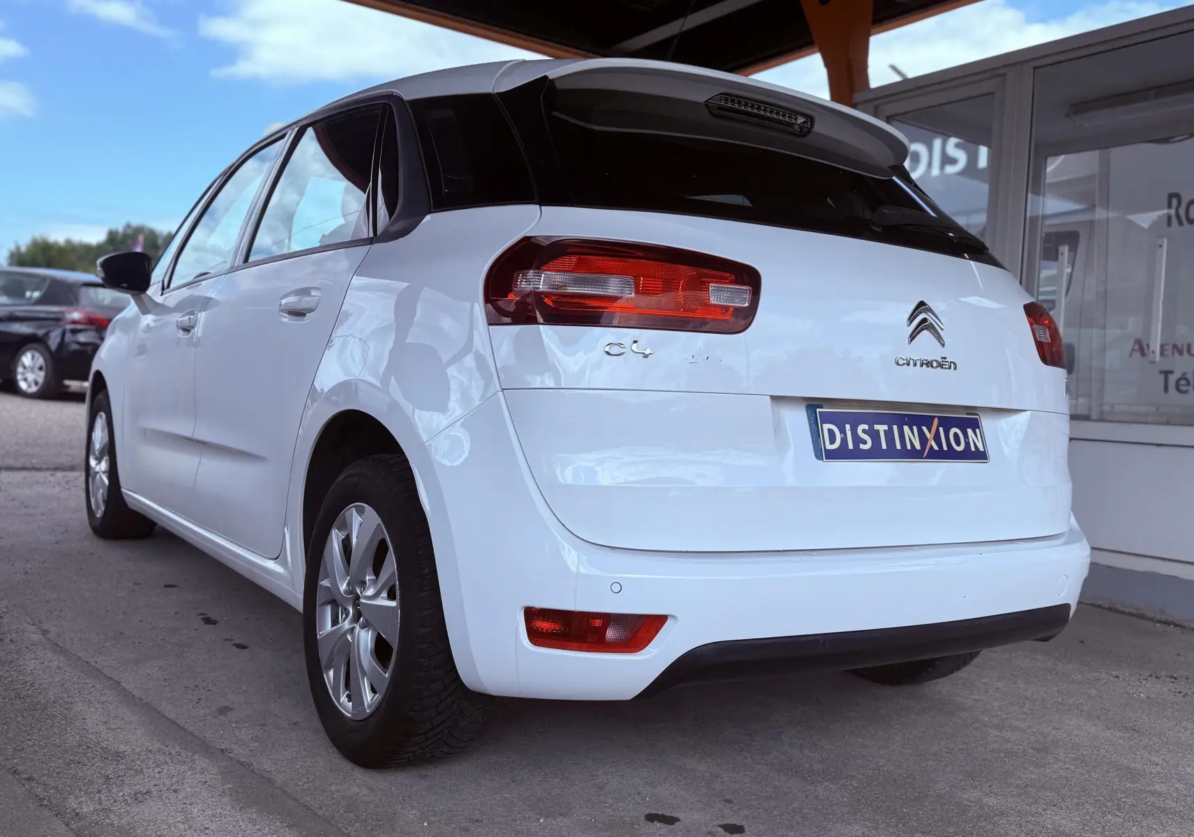 Vue 3/4 arrière gauche d'une Citroën C4 Picasso blanche de 2014 avec feux arrière rouges et toit noir contrasté.