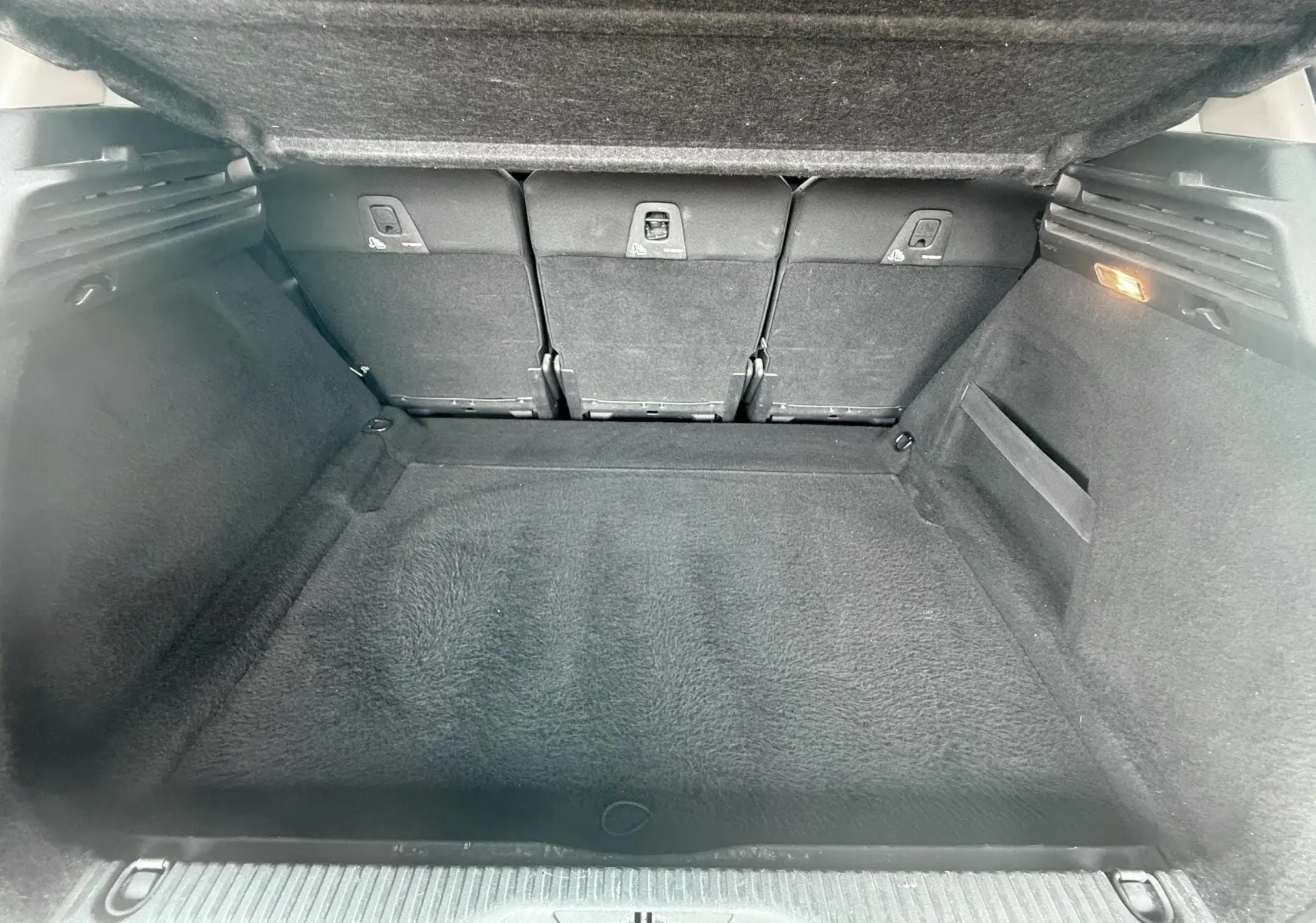 Coffre spacieux vu de l'intérieur arrière d'une Citroën C4 Picasso 2014 blanche, avec sièges arrière rabattables.