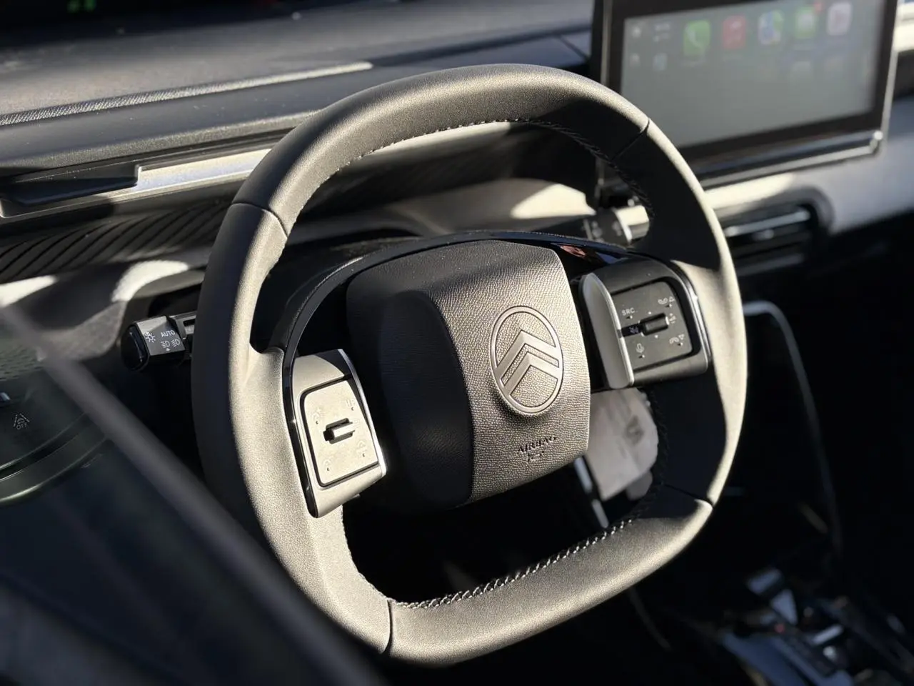 Gros plan sur le volant multifonctions noir du Citroën C3 Aircross Hybrid 2025 avec écran tactile en arrière-plan.