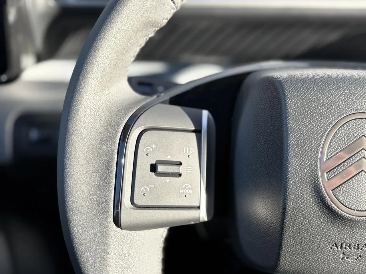 Gros plan sur les commandes gauche du volant gris du Citroën C3 Aircross Hybrid 2025 avec logo chrome visible.