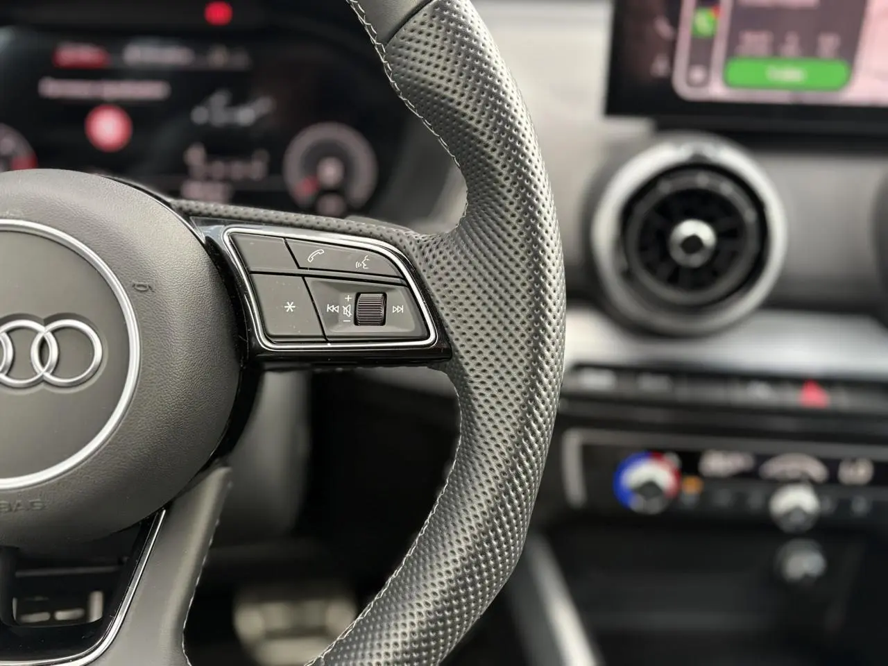 Gros plan sur le volant en cuir perforé de l’Audi Q2 rouge 2025, avec commandes multifonctions visibles.