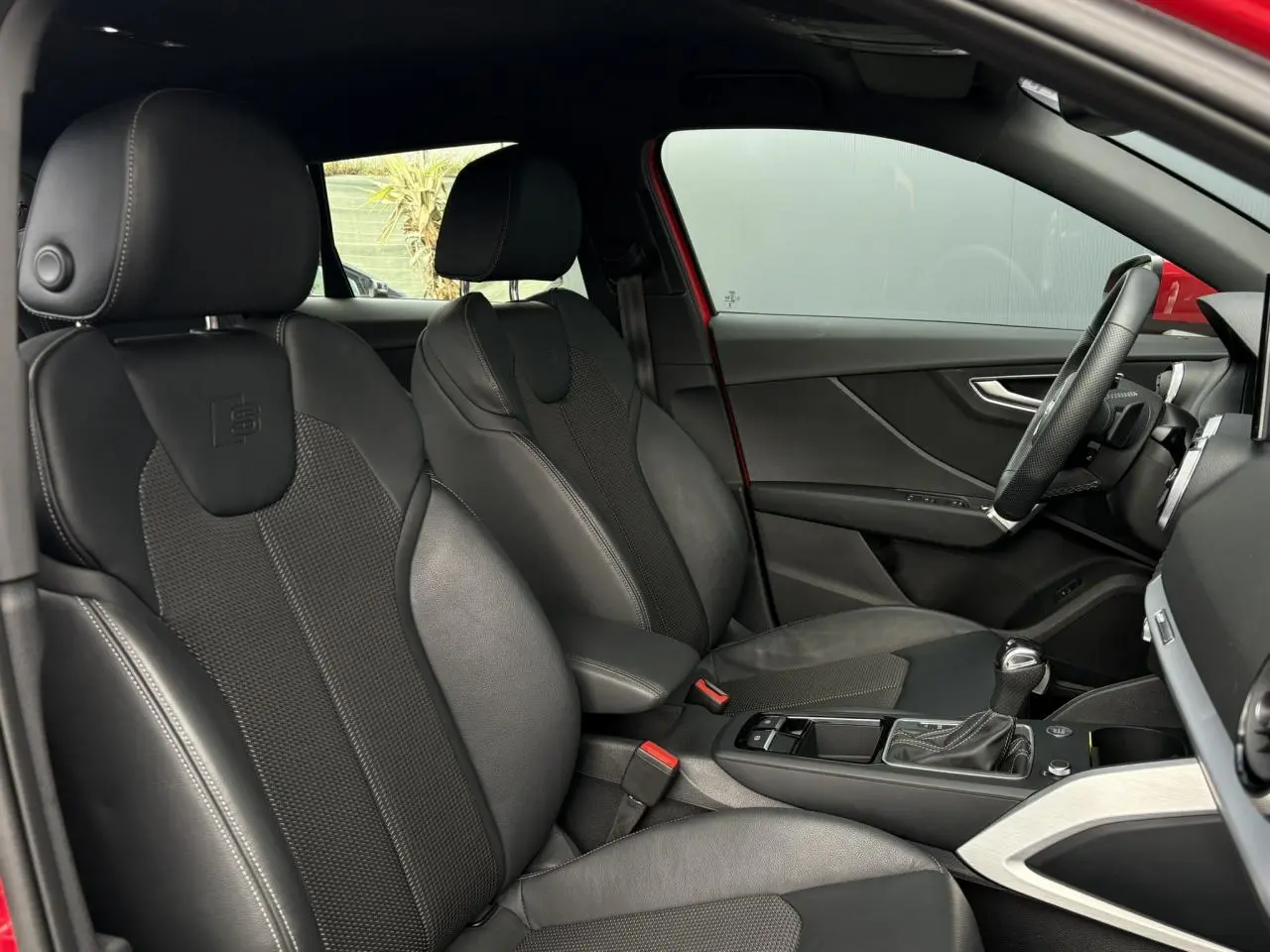 Vue intérieure côté conducteur de l'Audi Q2 rouge 2025, sièges sport cuir/tissu noirs avec logo S embossé.