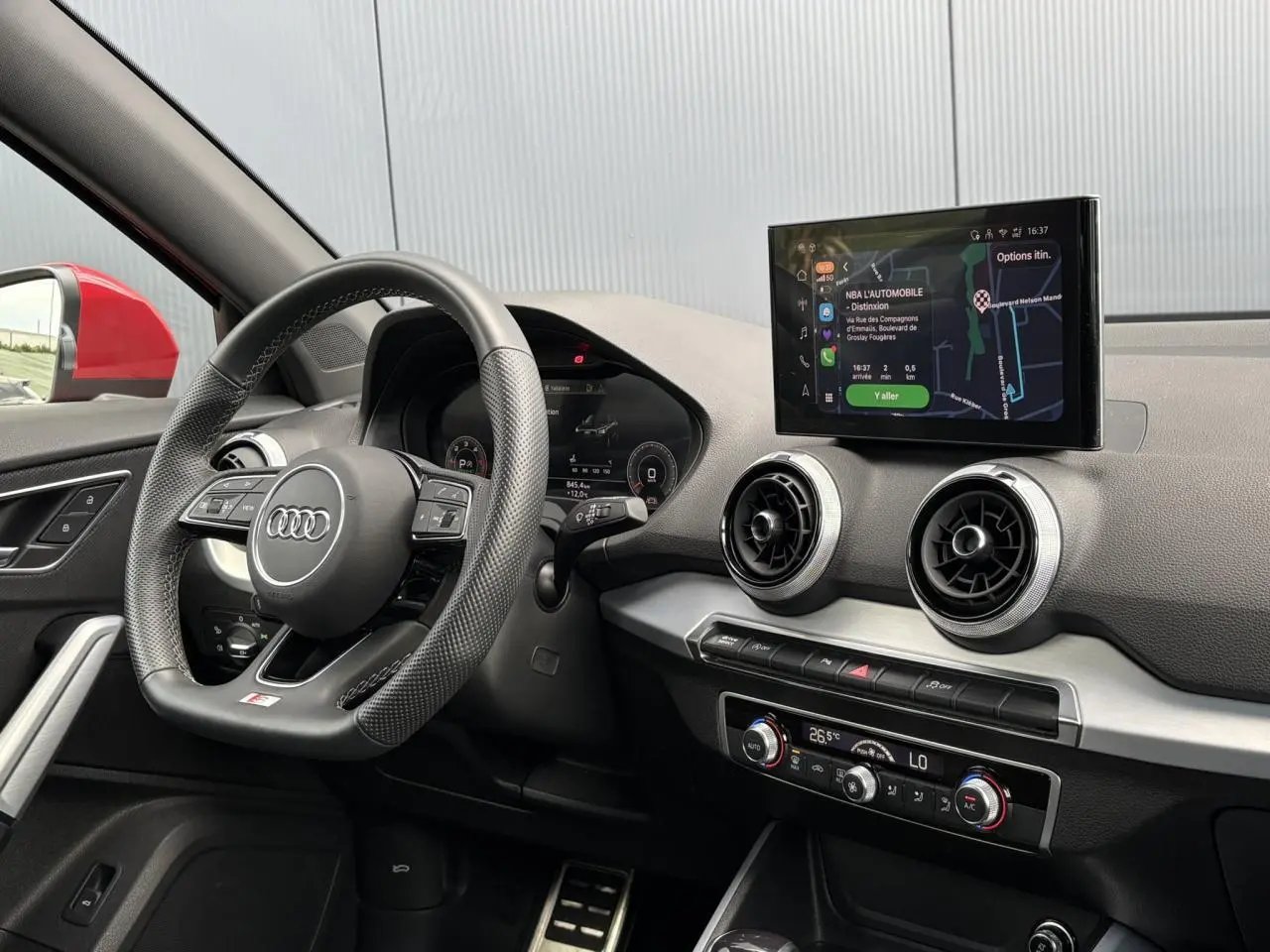 Vue intérieure côté conducteur de l’Audi Q2 rouge 2025, avec volant cuir multifonction et écran MMI navigation visible.