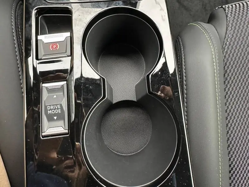 Gros plan sur la console centrale noire avec porte-gobelets et commandes Drive Mode du Peugeot 2008 hybride gris 2025.