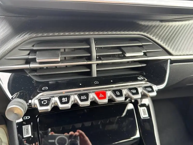 Gros plan sur la console centrale du Peugeot 2008 gris 2025, montrant les commandes climatisation et bouton d’alerte rouge.