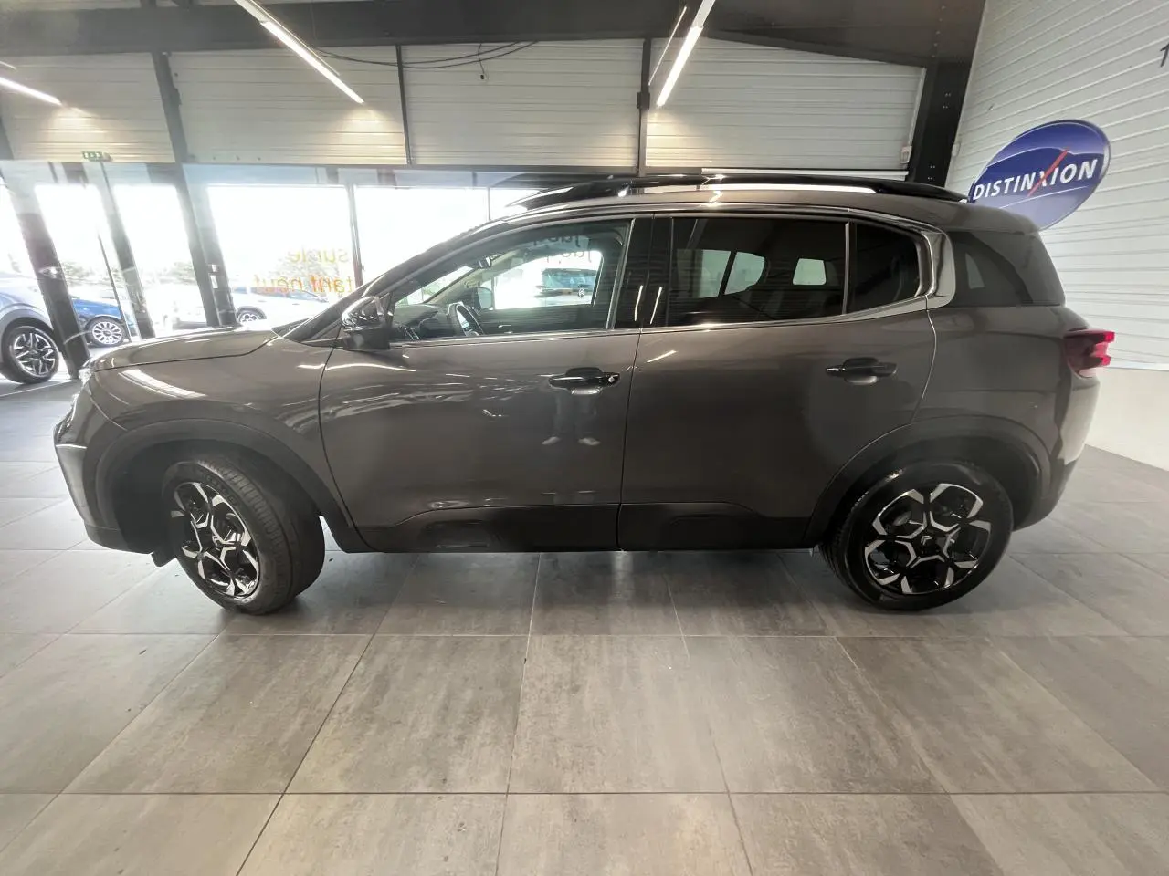 Vue latérale droite d'un Citroën C5 Aircross gris platinium avec jantes alliage 18'' bi-ton en intérieur showroom.