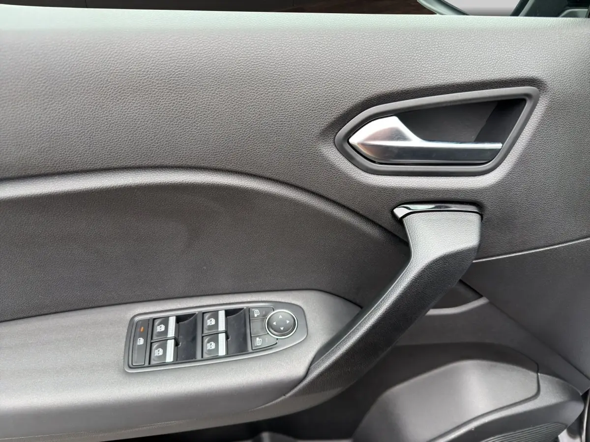 Vue rapprochée de la porte intérieure côté gauche de la Renault Symbioz noire, avec commandes électriques des vitres et poignée argentée.