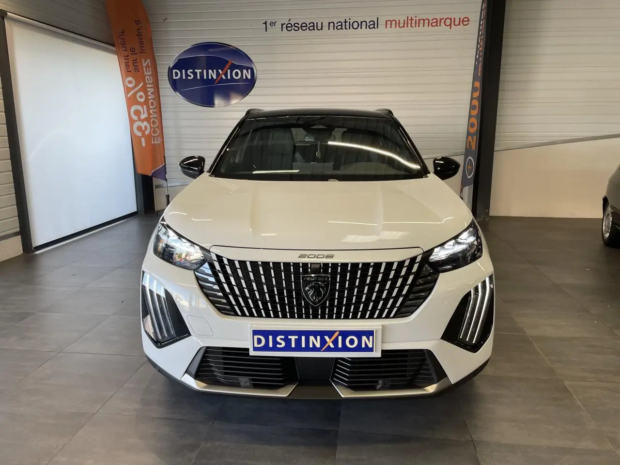 Vue frontale d'un Peugeot 2008 blanc avec calandre noire à motifs verticaux et feux LED en griffes, en intérieur showroom.