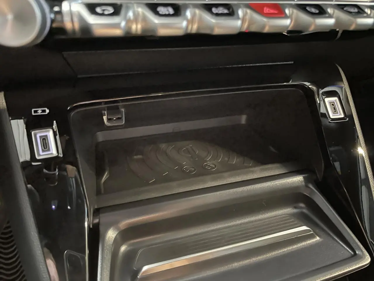 Gros plan sur la console centrale noire du Peugeot 2008 Hybrid 2026 avec chargeur à induction et prises USB type C.