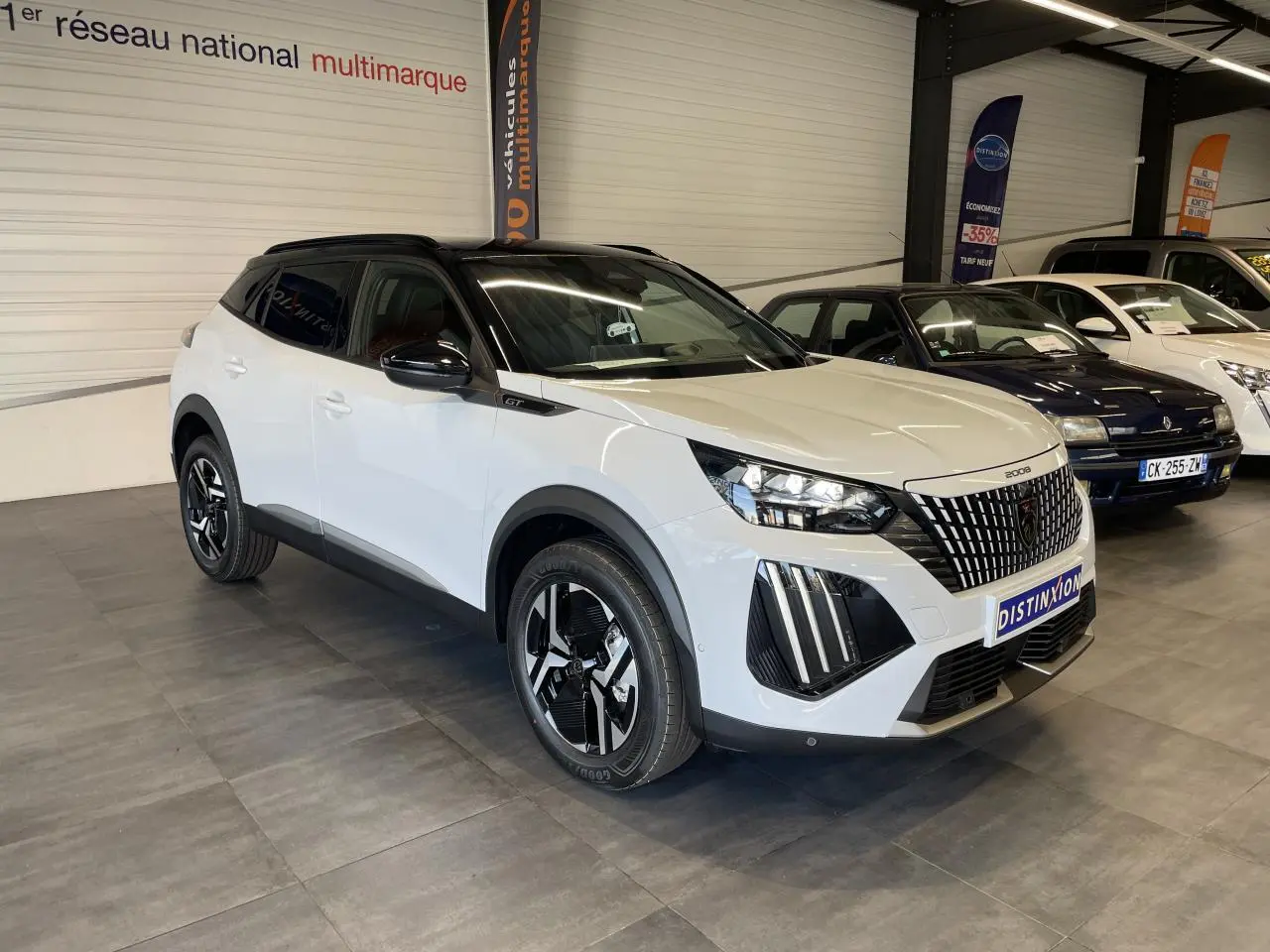 Peugeot 2008 hybride blanche vue 3/4 avant droit en intérieur, toit noir et calandre à liserés chromés.