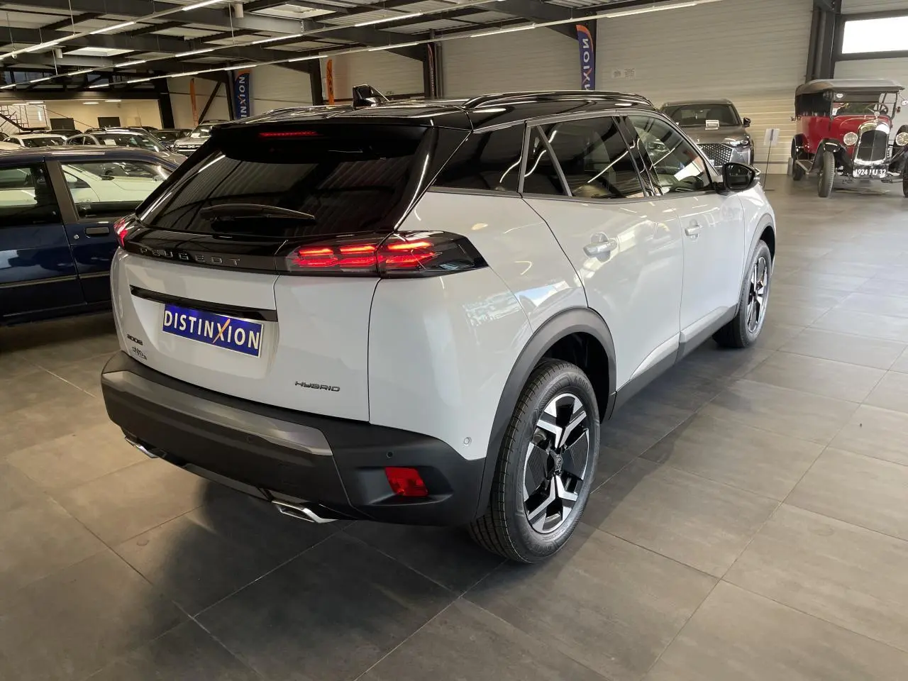 Vue 3/4 arrière droite du Peugeot 2008 blanc hybride avec toit noir et feux arrière LED en showroom.