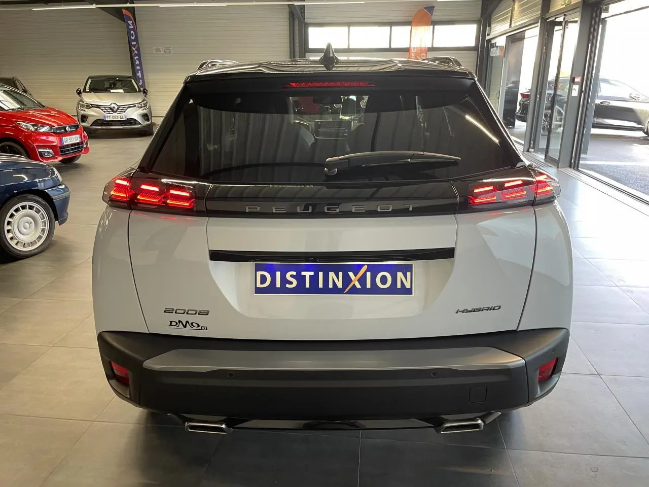 Vue arrière d'un Peugeot 2008 blanc hybride avec feux LED 3 griffes et double sortie d'échappement chromée en intérieur showroom.