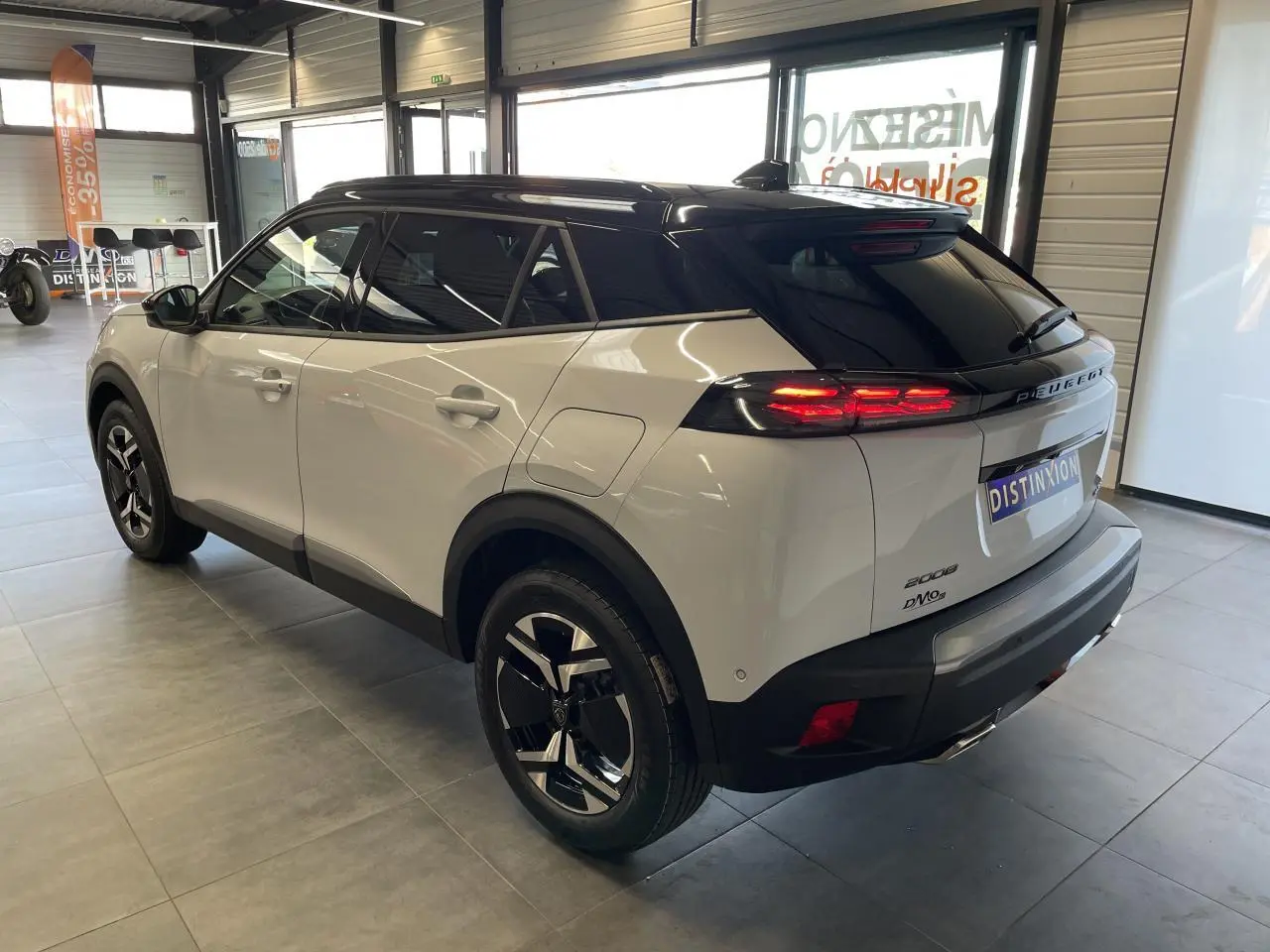 Peugeot 2008 blanc vue 3/4 arrière droit en intérieur avec toit noir et feux arrière LED allumés.