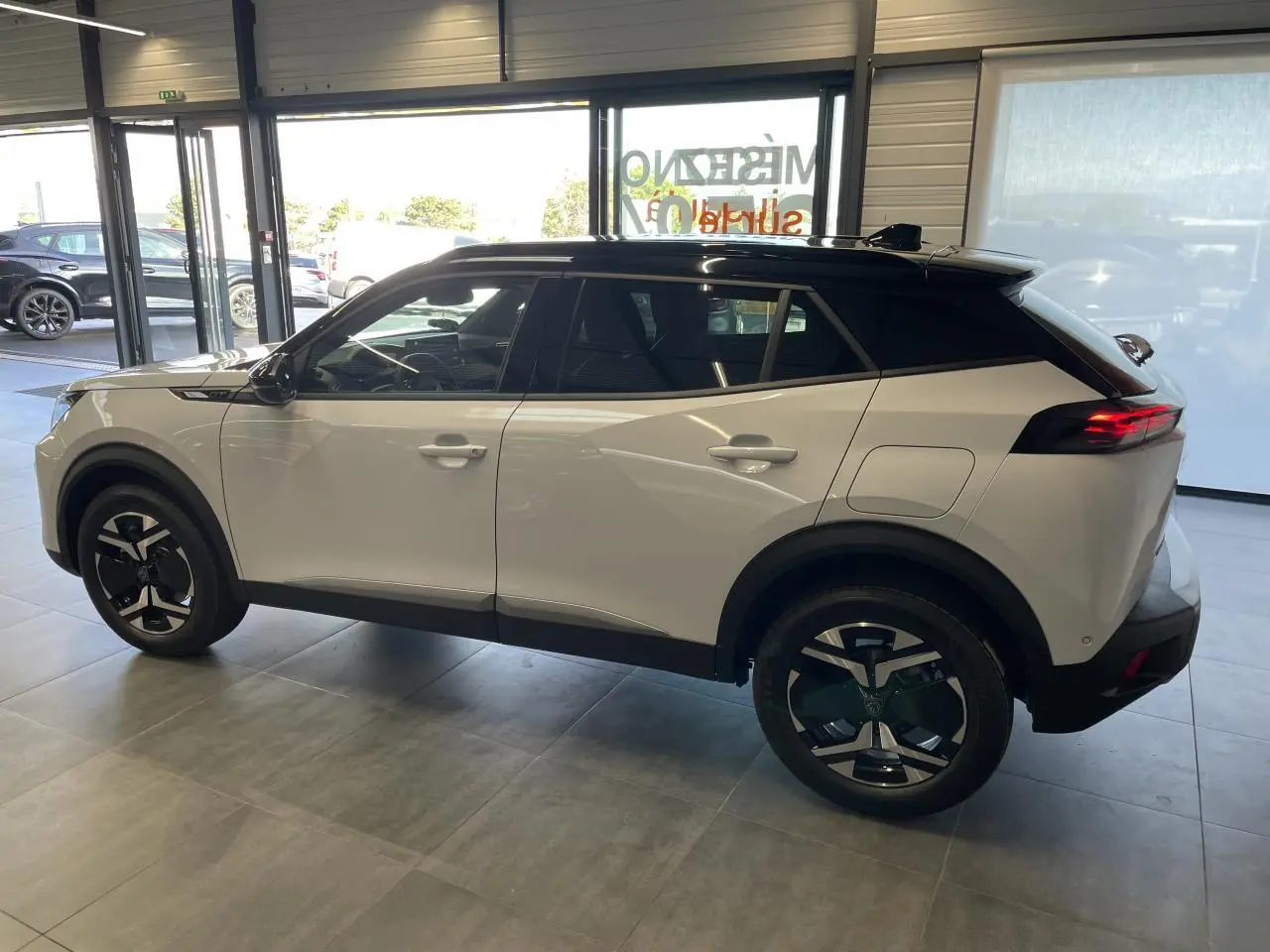 Peugeot 2008 blanc vue de profil côté gauche, toit noir et jantes alliage distinctives en concession.