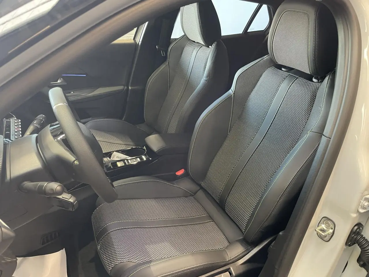 Vue intérieure côté conducteur du Peugeot 2008 blanc, mettant en valeur les sièges sport noirs avec surpiqûres claires.