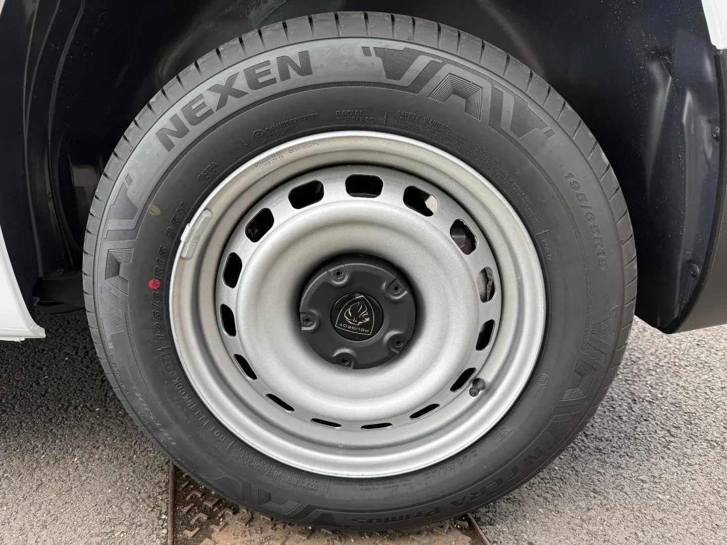 Gros plan sur la roue avant droite du Peugeot Partner blanc Icy, mettant en valeur la jante acier et le pneu Nexen.