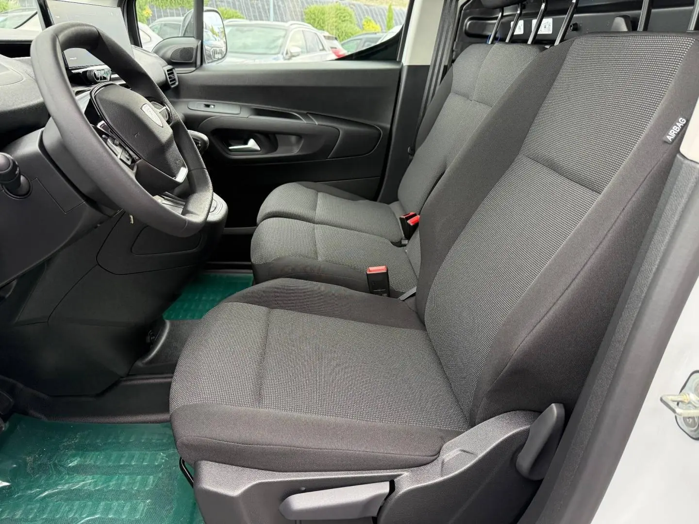 Vue intérieure côté conducteur du Peugeot Partner 2026, sièges tissu gris Curitiba Triton Meltem et volant multifonction.