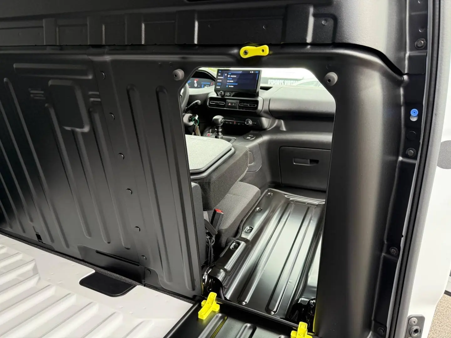 Vue intérieure par la porte latérale droite ouverte du Peugeot Partner blanc Icy, montrant la cloison et l'avant du poste de conduite.