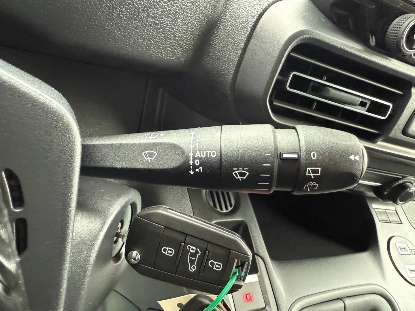 Gros plan sur la commande d’essuie-glace et la clé insérée dans le contacteur du tableau de bord noir du Peugeot Partner blanc Icy.
