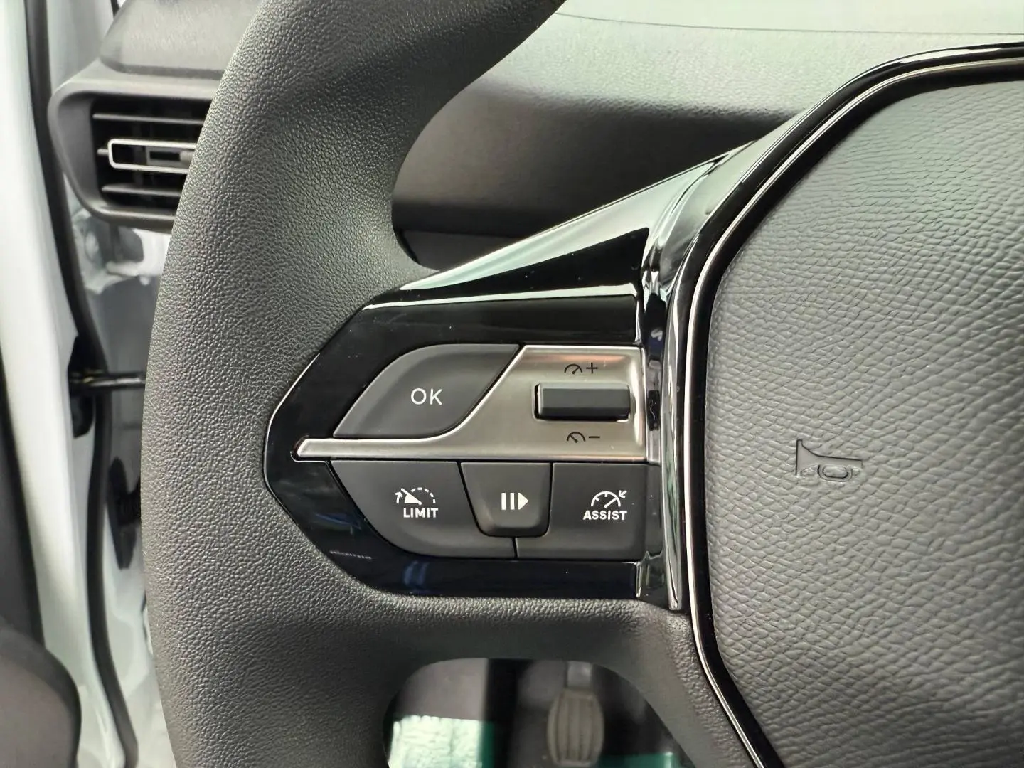 Gros plan sur le volant multifonction noir du Peugeot Partner blanc Icy, avec commandes de régulateur et assistance visibles.