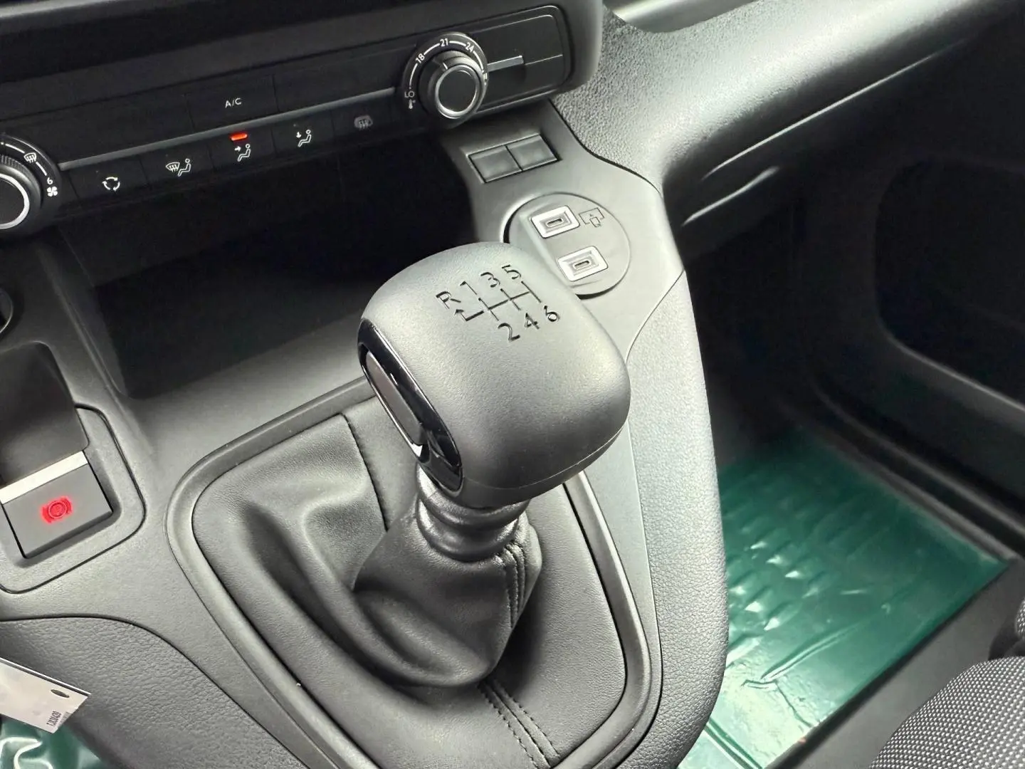 Gros plan sur le levier de vitesses manuel noir du Peugeot Partner 2026, avec console centrale et commandes clim visibles.
