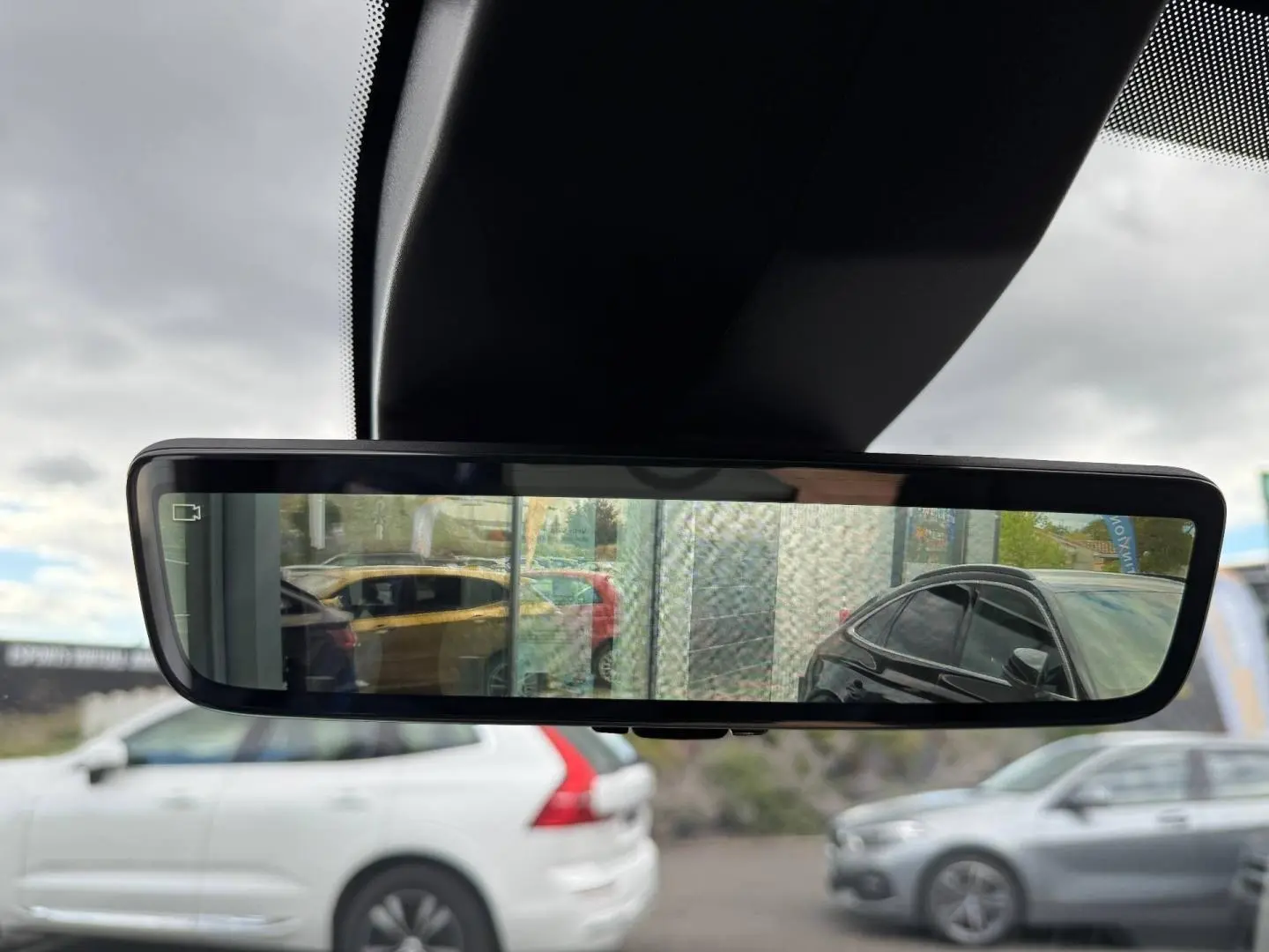 Rétroviseur intérieur numérique montrant plusieurs véhicules stationnés, avec reflet d'une voiture noire à droite.