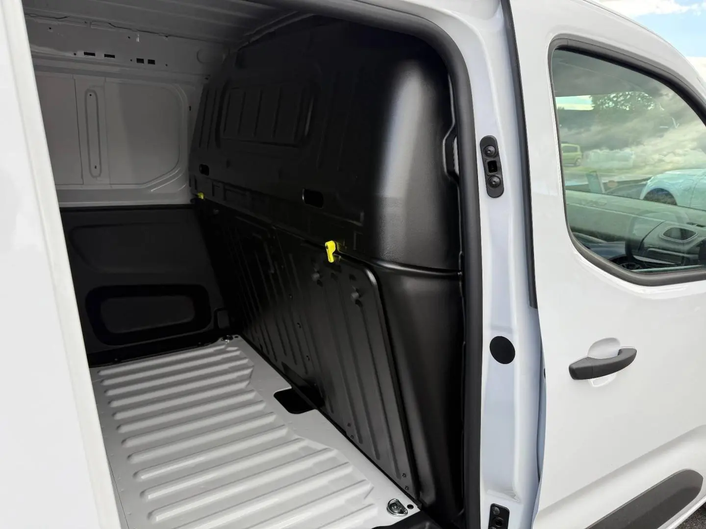 Vue intérieure côté droit du coffre d'un Peugeot Partner blanc Icy avec cloison pleine noire et porte latérale coulissante ouverte.