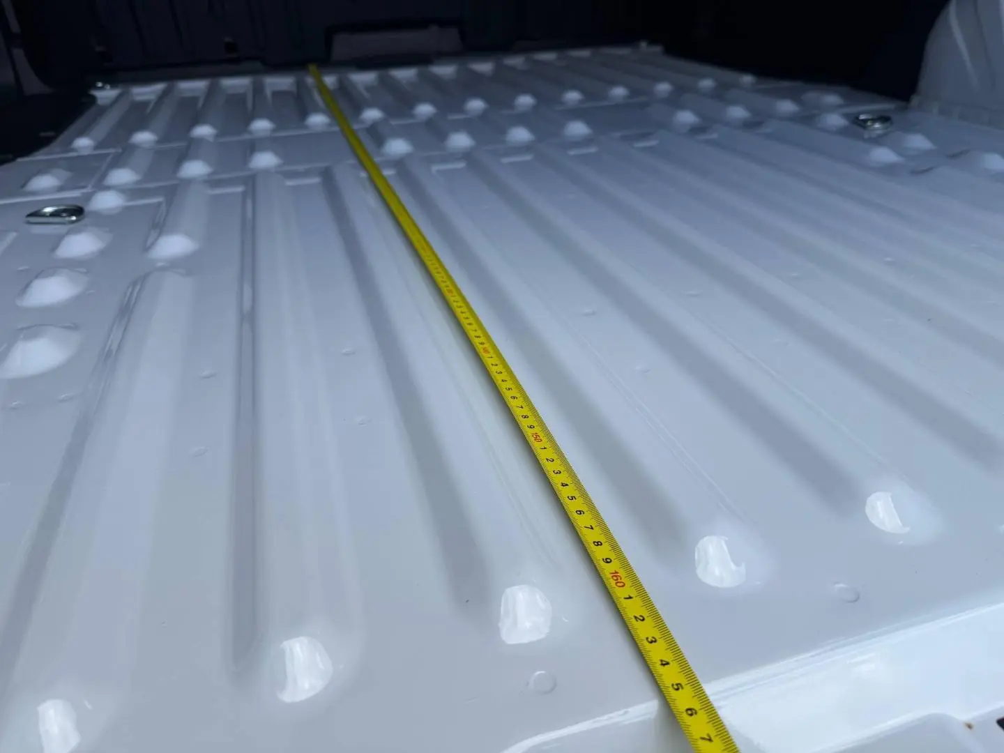 Gros plan sur la surface blanche Icy du plancher de chargement du Peugeot Partner avec un mètre ruban jaune posé dessus.