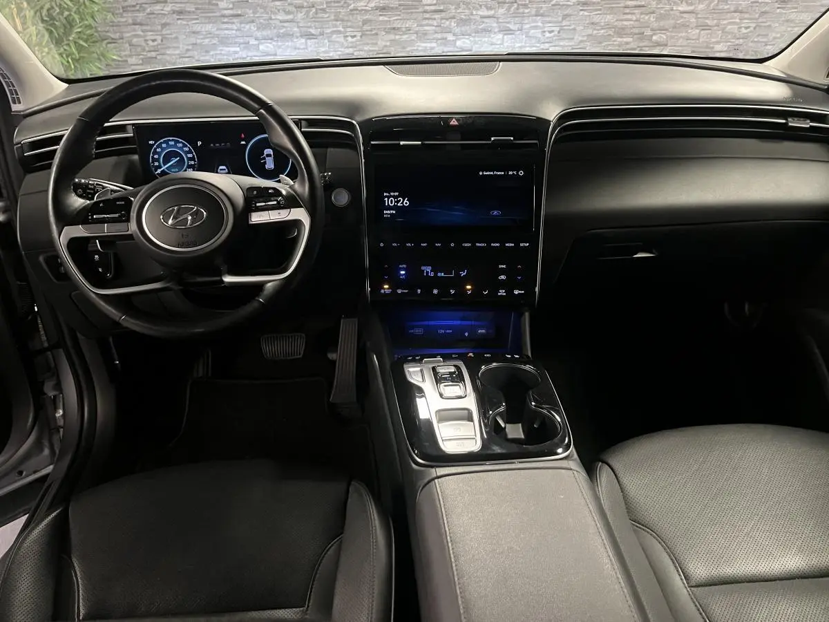 Intérieur du Hyundai Tucson 2023 vu de face, tableau de bord noir avec écran tactile central et volant cuir.