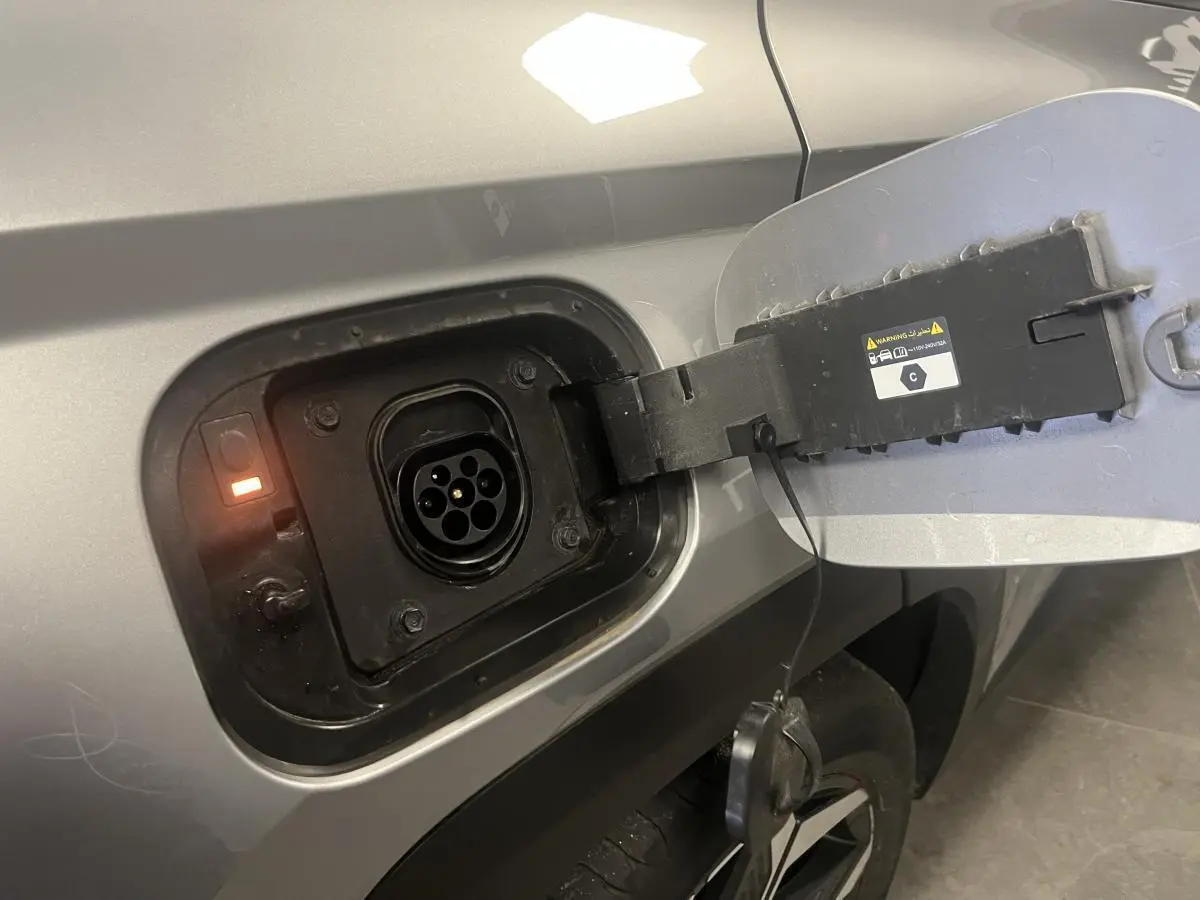 Prise de recharge ouverte côté gauche d’un Hyundai Tucson gris 2023 hybride rechargeable, avec témoin lumineux orange.
