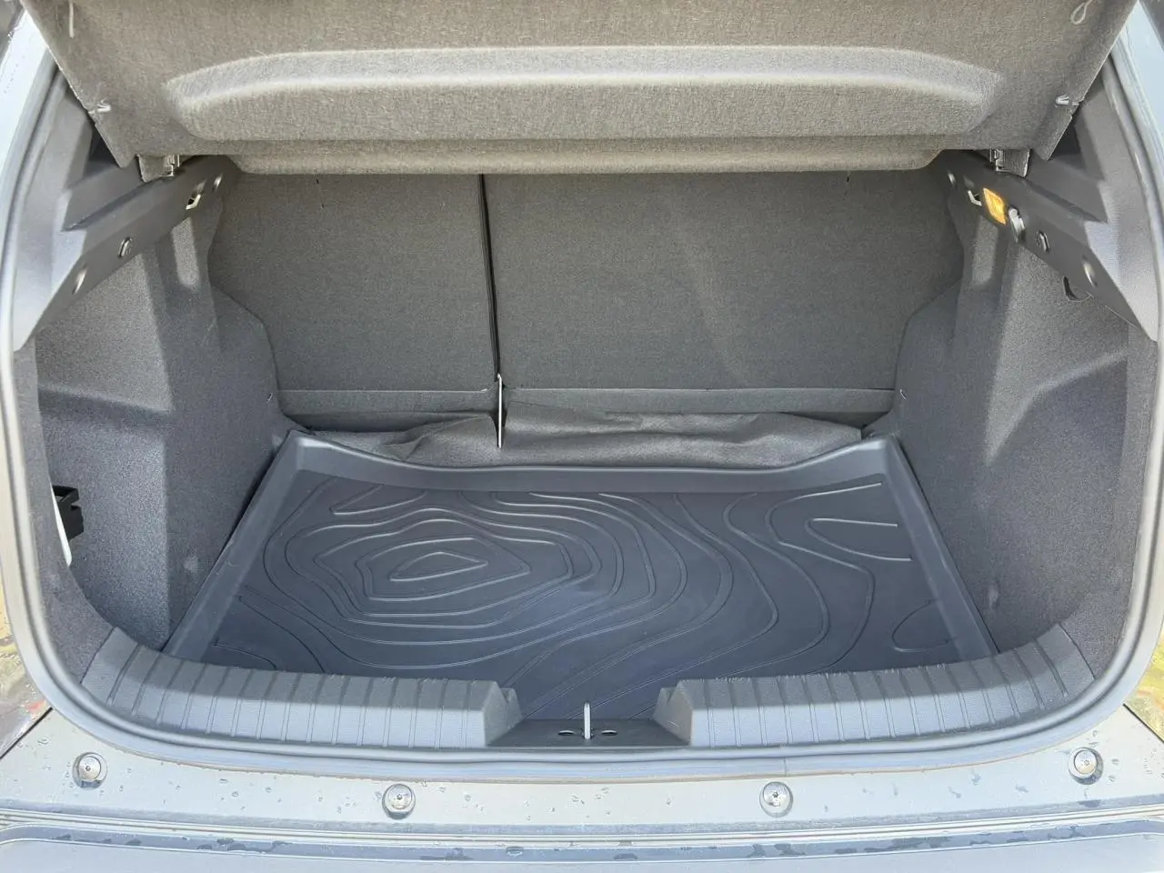 Coffre ouvert vu de l'arrière d'un Dacia Duster 2025 noir nacré avec tapis de protection en caoutchouc.