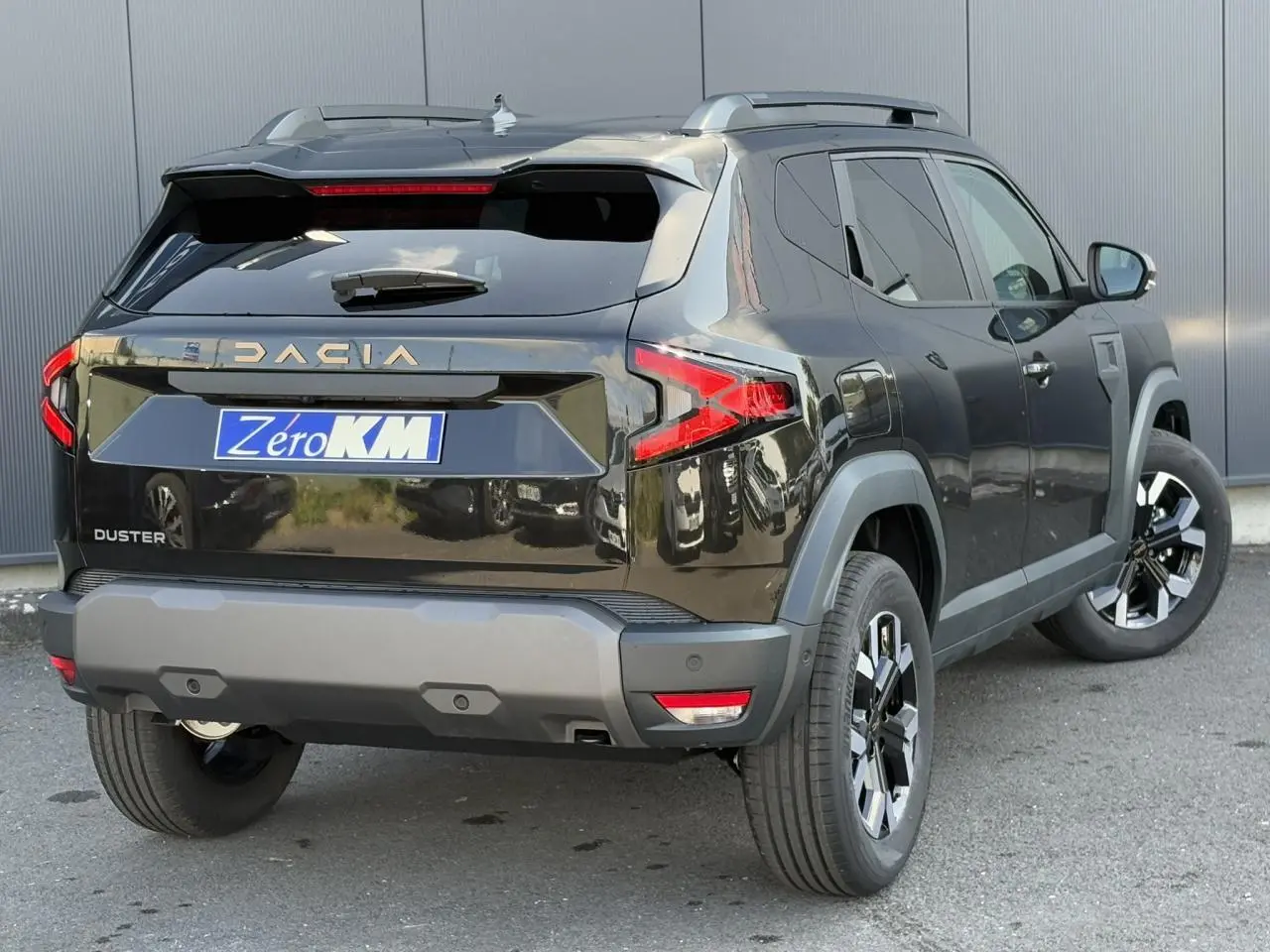 Vue 3/4 arrière droite d'un Dacia Duster noir nacré avec barres de toit et jantes alliage 17 pouces.