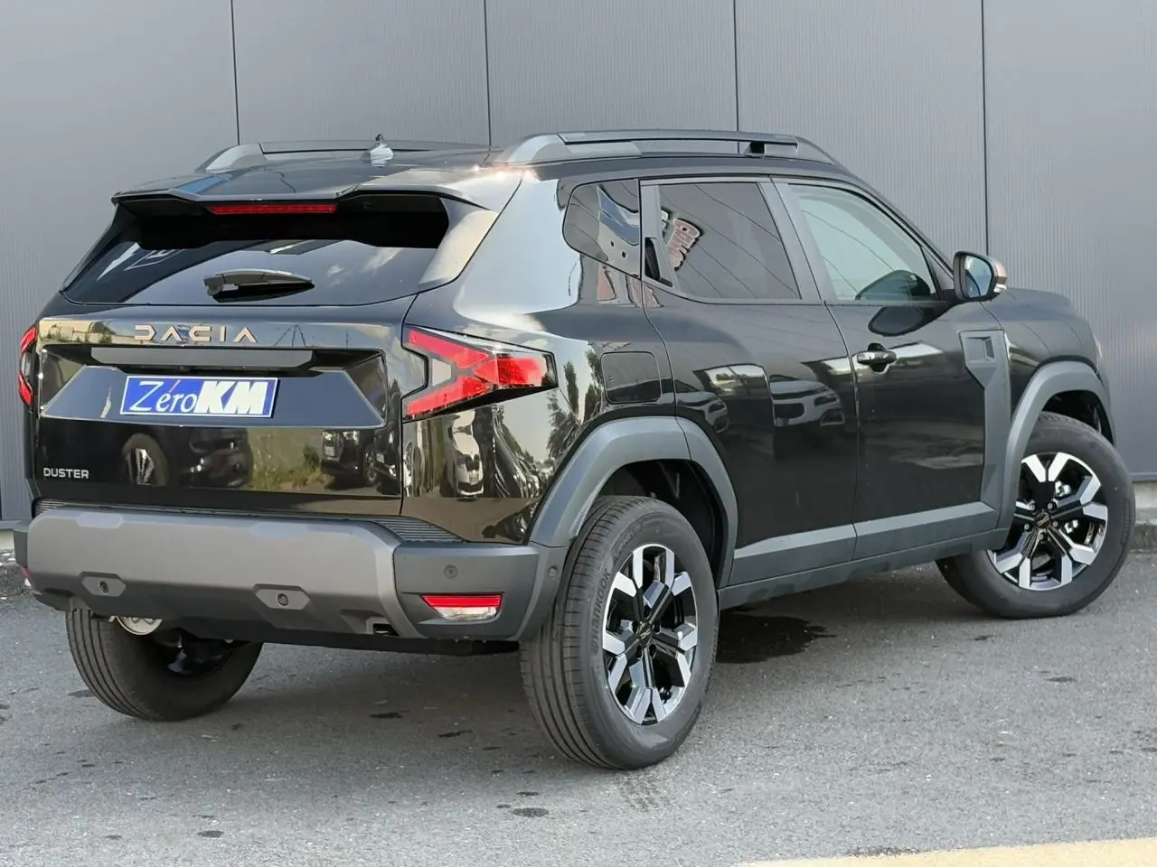 Vue 3/4 arrière droite du Dacia Duster 2025 noir nacré avec barres de toit et jantes alliage bicolores.
