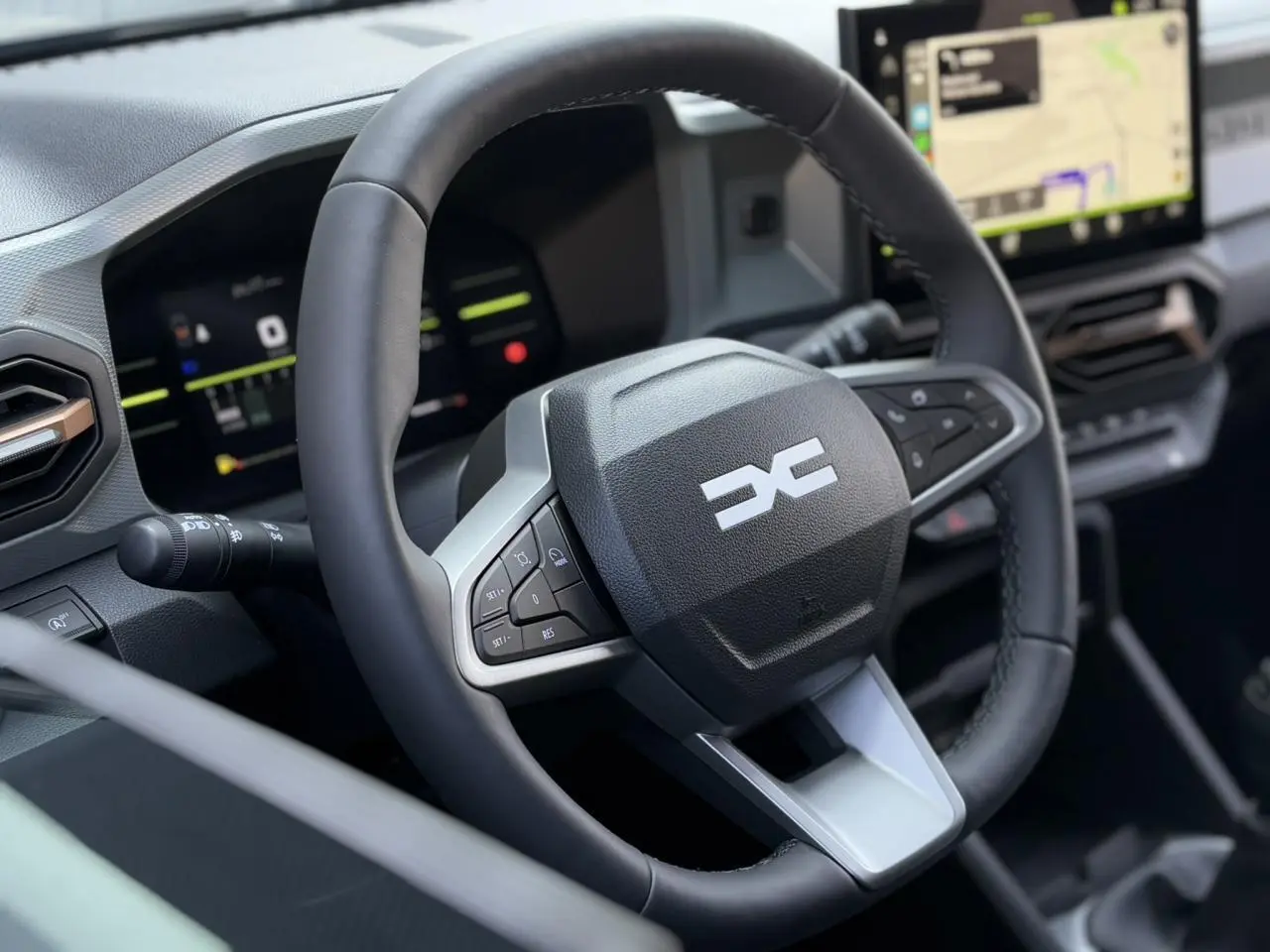 Gros plan sur le volant multifonction noir du Dacia Duster 2025 avec tableau de bord digital et écran GPS tactile.