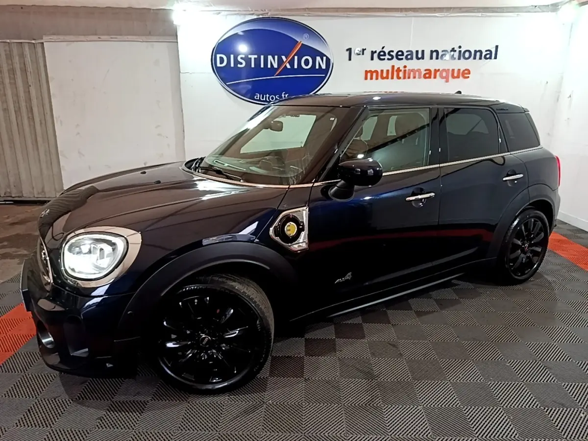 Vue 3/4 avant droit d'une MINI Countryman Cooper SE bleu foncé avec jantes noires et toit noir dans un showroom.