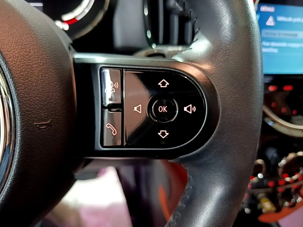 Gros plan sur les commandes au volant cuir noir de la MINI COUNTRYMAN hybride rechargeable 2021, avec écran tactile en arrière-plan.