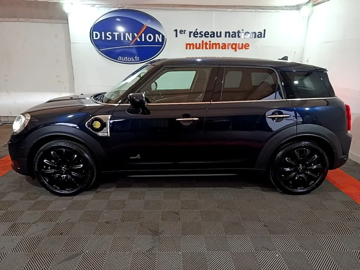 Profil côté gauche d'un MINI Countryman Cooper SE bleu avec jantes noires et badge hybride visible sur l'aile avant.
