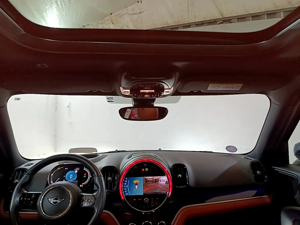 Intérieur du MINI Countryman Cooper SE 2021, vue tableau de bord avec écran central circulaire et volant cuir noir.