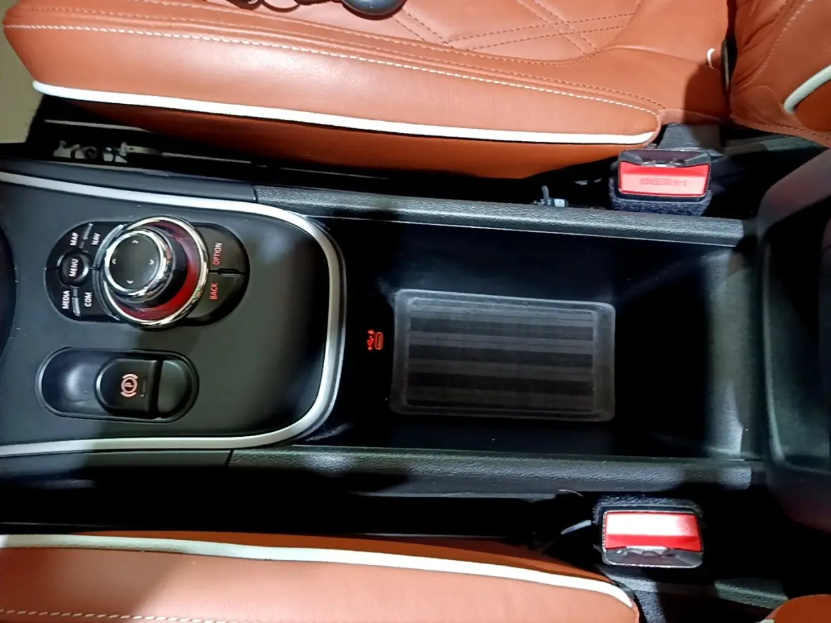 Vue rapprochée de la console centrale noire avec molette de commande et sièges en cuir marron clair du MINI Countryman hybride.